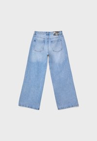 Vue arrière d'un jean bleu clair à jambes larges avec deux poches arrière et une étiquette noire sur la ceinture, sur fond uni.
