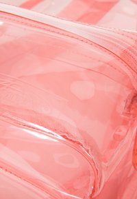 Klar rosa plastpåse med vita prickar, med dragkedja och slät yta. Orange dragkedja ger kontrast.