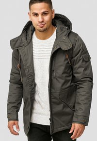 Dark green, padded parka jacket with a hood, front zipper, side pockets, and adjustable cuffs. Features contrasting brown hardware accents.