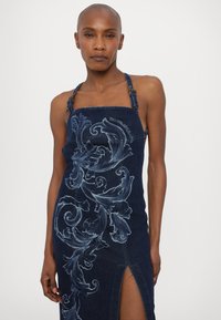 Τζιν φόρεμα με μπλε λουλουδένια κεντήματα, λουριά halter, εφαρμοστή �σιλουέτα, σκίσιμο μέχρι τον μηρό και σκούρο βερνίκι.