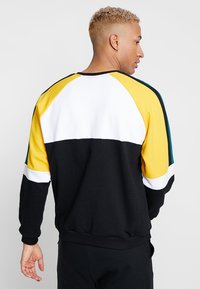 Sweatshirt preto de pulôver com design em blocos de cor; inclui detalhes em amarelo, branco e verde-água, com punhos e cintura canelados.
