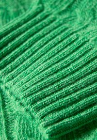 Tejido verde de punto con una prominente textura acanalada, que muestra una superficie suave y peluda. Color vibrante con sutiles variaciones en la tonalidad.