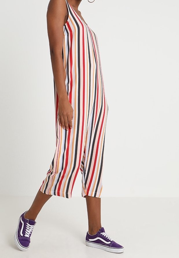 Une combinaison sans manches à rayures verticales rouges, noires, orange et blanches. Portée avec des baskets violettes, longueur cheville et coupe décontractée.