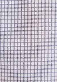 Tissu blanc avec un motif en grille de petits carrés bleus et noirs cousus, espacés uniformément.