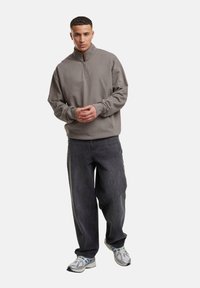 Pull en polaire gris discret, avec un col montant à fermeture éclair. Associé à un jean ample de couleur foncée et des baskets réfléchissantes.
