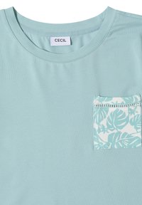 T-shirt bleu clair à col rond avec une poche poitrine à motif de feuilles tropicales blanches et bleues et une étiquette portant la mention CECIL à l'intérieur du col.