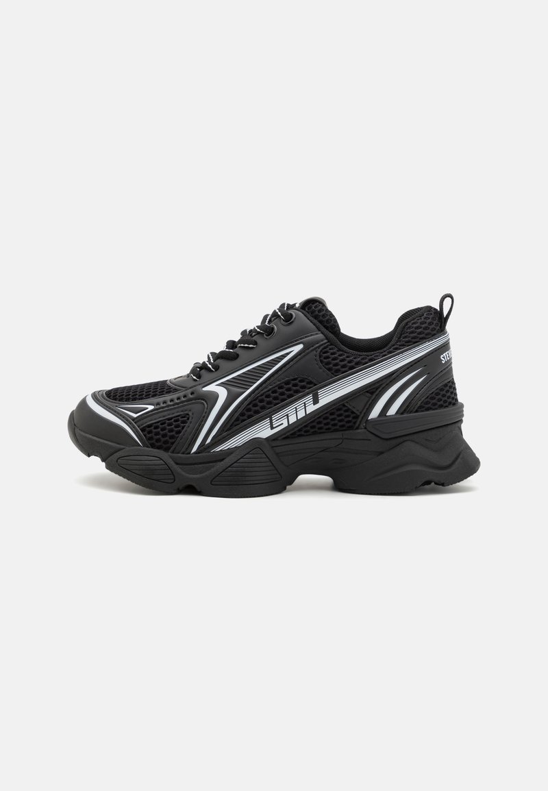 Zapatos deportivos negros con parte superior de malla, acentos blancos, suela gruesa y forma redondeada. Cuenta con cordones y una lengüeta en el talón.