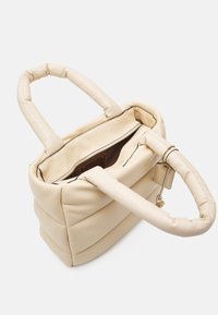 Beżowa pikowana torebka z dwoma krótkimi uchwytami, zamkiem błyskawicznym oraz kieszenią wewnętrzną. Gładka faktura z kontrastującym czarnym przeszyciem i metką.