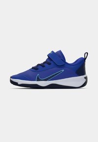 Zapatilla deportiva azul con parte superior texturizada, correa de velcro, cordones y una suela intermedia blanca con detalles en verde y un talón estampado.