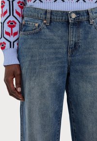 Vaqueros azul oscuro con corte de pernera recta, con detalles de botones de cobre y diseño de cinco bolsillos. La textura parece suave y ligeramente descolorida.