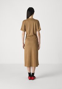 Rochie maro, până la genunchi, cu mâneci rulată și talie strânsă. Purată cu șosete negre și pantofi roșii, văzută din spate.