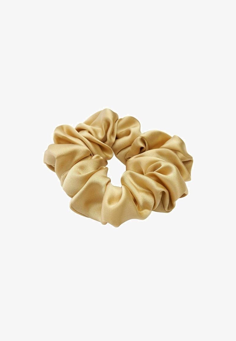 Chouchou en satin doré avec tissu lisse et froncé formant un accessoire circulaire pour cheveux sur fond blanc.