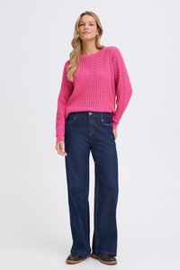 Un pull en tricot rose avec un motif texturé, associé à un jean en denim sombre à jambes larges. Stylé avec des bottes marron et une ceinture simple.