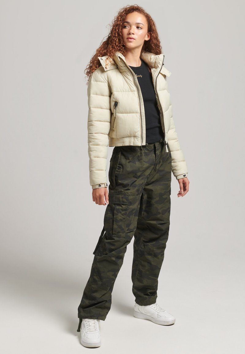 Giacca puffer cropped crema, polsini a coste, top nero, pantaloni cargo mimetici, sneakers bianche, leggero lucido sul tessuto, due tasche laterali sulla giacca.