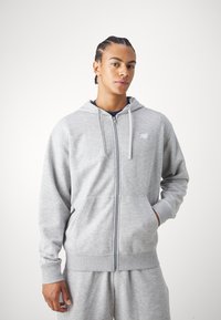 Grå zip-up hoodie lavet af blødt stof, med en forlommek og snoretræk i hætten. Vist med matchende grå shorts.