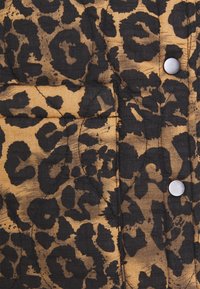 Vatterat tyg med ett mönster i tan och svart leopardprint, med silverfärgade tryckknappar och strukturerad yta.