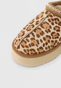 Gros plan sur une pantoufle mocassin à imprimé léopard avec une semelle beige et des coutures visibles sur la partie supérieure avant.