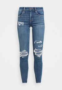 Jeans de mezclilla azul delgados con detalles desgastados. Presenta desgarros en las rodillas, un diseño clásico de cinco bolsillos y un cierre de botón.