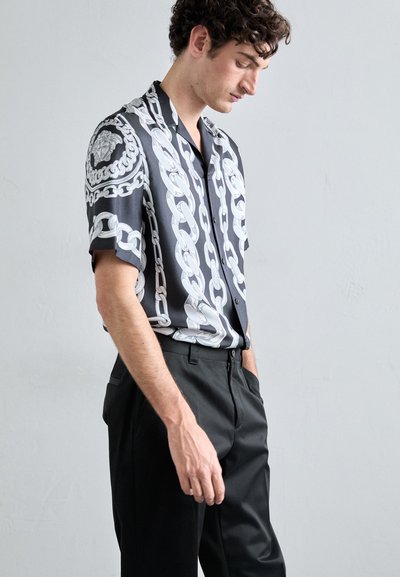 Short-sleeved black shirt with a white chain pattern. Features a button-up design and smooth fabric. Paired with classic black trousers.