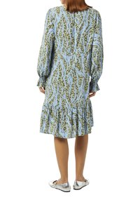 Langwerpige jurk met lange mouwen en een gerimpelde onderkant, met een groen en blauw abstract patroon. Gecombineerd met glanzende zilveren ballerina's.