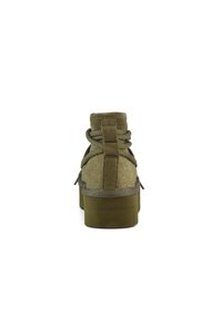 Botines de ante verde oliva con superficie texturizada, punta redondeada y suela de goma gruesa y sólida. Presentan cordones y una lengüeta.