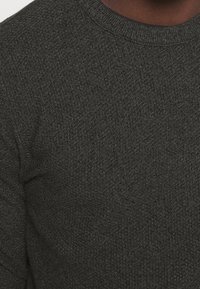 Pull en tricot gris foncé avec un col rond et un motif de tissu texturé, adapté pour un port décontracté ou en superposition.