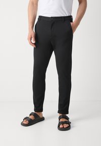 Czarne dopasowane spodnie z zapięciem na guzik i szlufkami na pasek. Noszone z czarnymi sandałami z teksturowanym paskiem i otwartym noskiem.