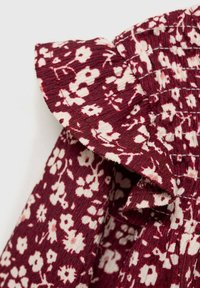 Burgundi kangas, millel on valge lillemuster, rippuva äärega. Tekstuuriga pind, mis sisaldab kogutud disaini. Lähedane vaade käiste detailile.