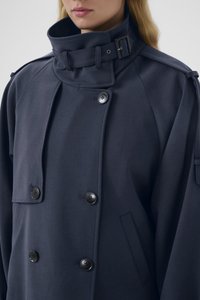 Marineblå dobbeltspent frakk laget av ullblanding, med høy krage, store knapper og en sidelomme med glatt tekstur.