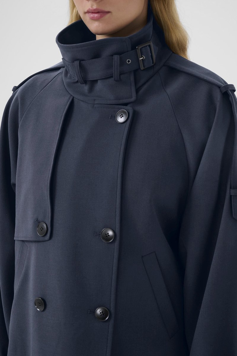 Manteau bleu marine à double boutonnage en mélange de laine, doté d'un col montant, de gros boutons et d'une poche latérale avec une texture lisse.