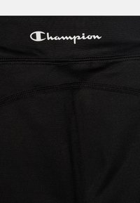 Fekete sportnadrág sima anyagból, varrott részletekkel és fehér "Champion" logóval a derékrészen.