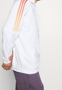 Witte hoodie met een voorzak, voorzien van drie verlopen strepen in rood en oranje langs de linker mouw. Gestructureerd materiaal, casual pasvorm.