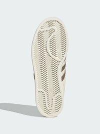 Biela podrážka tenisky so štruktúrovaným vzorom rybej kosti. Má hnedé detaily a zaoblené okraje. Logo je viditeľné v oblasti päty.