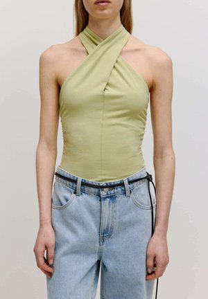 Hellgrüner ärmelloser Bodysuit mit einem Halterneck-Design. Kombiniert mit hoch taillierten, hellblauen Jeans aus Denim und einem schwarzen Gürtel.