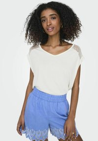 Luźna biała koszulka z dekoltem w kształcie litery V oraz siateczkowymi detalami na ramionach, zestawiona z jasnoniebieskimi szortami z koronkowym wykończeniem dołu.