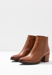 Ruskeat nahkaiset nilkkurit, joissa on tyylikäs muotoilu, terävä kärki ja matala lohkokorko. Sileä pinta, jossa hienovaraiset ompelu-yksityiskohdat.