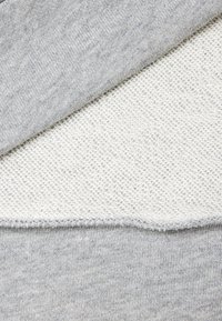 Tessuto grigio chiaro sovrapposto a tessuto bianco testurizzato, con una finitura liscia e un motivo sottile nel grigio. I bordi sono cuciti in modo pulito.