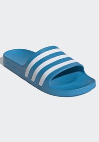 Blauwe schuimslipper gemaakt van gestructureerd synthetisch materiaal, met drie witte horizontale strepen op de bovenkant en een platte zool.