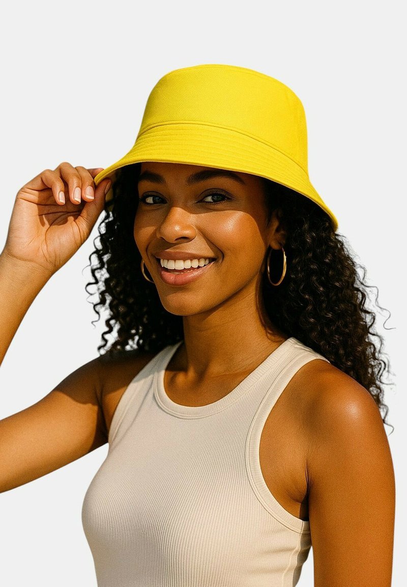 Geel emmerhoedje met een gestructureerde rand en een glad katoenen textuur. Model draagt een licht mouwloos topje, waarbij de schouders en krullen zichtbaar zijn.