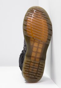 Suela de sneaker negra con un diseño de goma texturizada, con un agarre estampado y detalles transparentes cerca del dedo del pie. Marca visible en detalle.