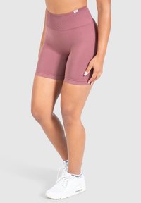 Pantalones cortos deportivos de talle alto en color malva con una cinturilla elástica y acanalada y una textura suave. Combinados con zapatillas blancas y calcetines hasta el tobillo.