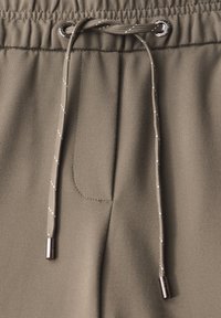Olijfgroene joggers met een gladde textuur, elastische tailleband en trekkoord. Voorzien van zilveren punten op het trekkoord en een voorzak.