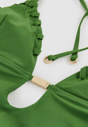 Roheline bikiini ülaosa, millel on sile tekstuur, lace-up detailid, kuldne riistvara ja reguleeritavad rihmad. Kujundatud lõikega detailiga.