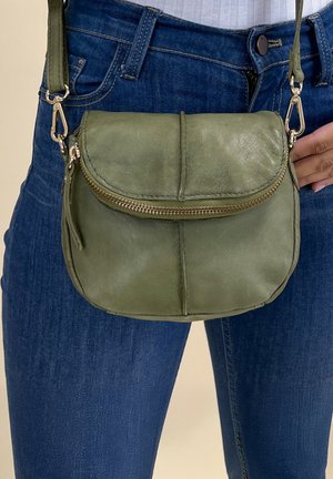 Zelena kožna torba za preklapanje s okruglim oblikom, zatvaranjem na zatvarač i metalnim akcentima. Ima prednji poklopac i teksturiranu površinu.