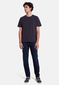 T-shirt in cotone blu scuro a girocollo con maniche corte, abbinata a jeans blu scuro aderenti e scarpe da ginnastica grigie con suole bianche.