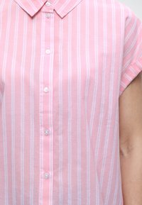 Ροζ πουκάμισο με κοντά μανίκια και κουμπιά, με λευκές κάθετες ρίγες, στη μέση και το χέρι ενός ατόμου.