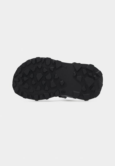 Μαύρη καουτσούκ σόλα με βαθύ, ακανόνιστο ανάγλυφο πέλμα σχεδιασμένο για πρόσφυση σε υπαίθριες επιφάνειες.