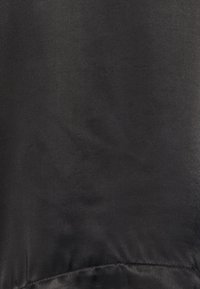 Tessuto di raso nero con una trama liscia, che mostra una lucentezza sottile e una leggera caduta. Presenta un orlo cucito lungo il bordo inferiore.