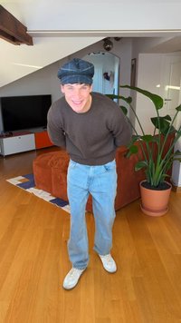 Casual outfit featuring a dark sweater, blue denim jeans, white sneakers, and a blue patterned cap in a brightly lit indoor setting.