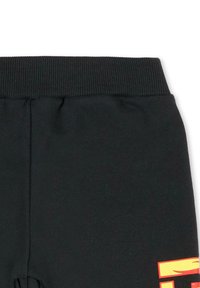 Zwarte, geribbelde tailleband van joggingbroek met een gladde textuur. Heeft een grote geel-oranje afbeelding aan de linkerkant.